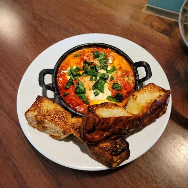Shakshuka in a black cast iron pan with toasted bread on a white plate.