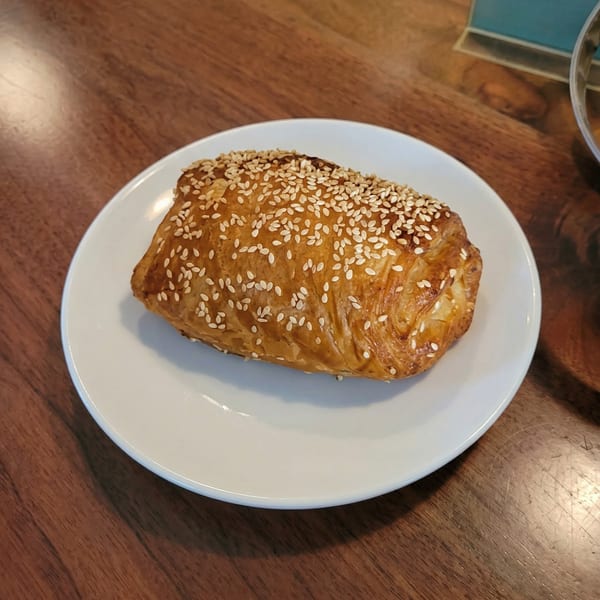 Golden-brown pastry sprinkled with sesame seeds on a white plate, resting on a wooden table.