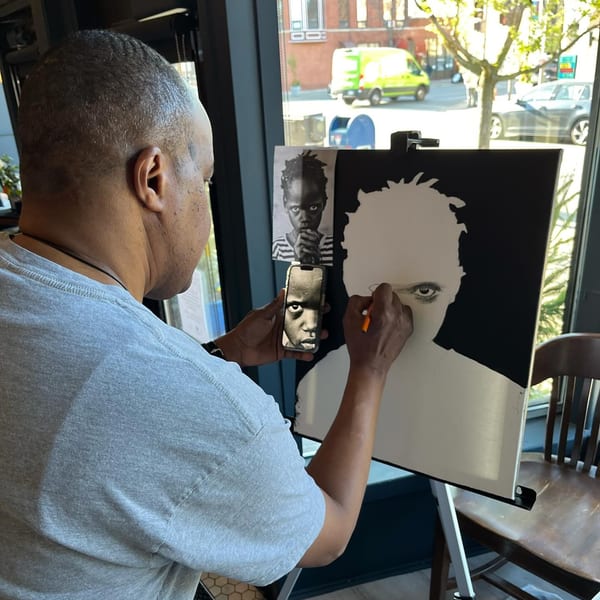 An artist sketches a portrait of a child from a reference image on his phone.