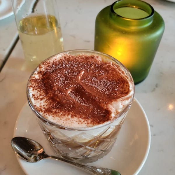 A dessert in a cut glass cup with whipped cream, cocoa powder, and sugar, next to a green candle.