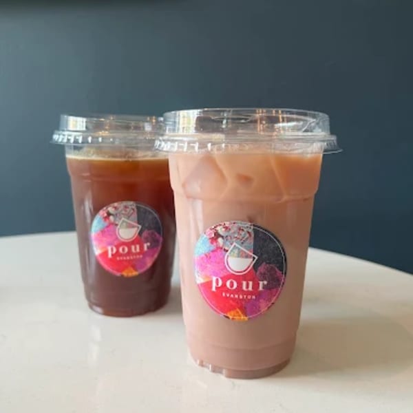 Two iced drinks from Pour Evanston, one dark and one light pink, on a white table.