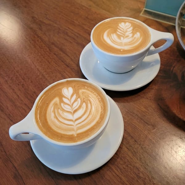 Two white cups of latte with intricate foam art sit on a wooden table.