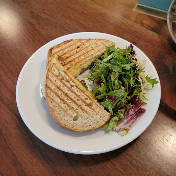 Grilled cheese sandwich with melted cheese and a side salad on a white plate.