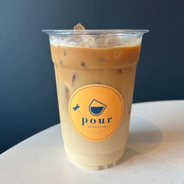 Iced coffee with milk and ice in a clear plastic cup with a yellow Pour Evanston logo.